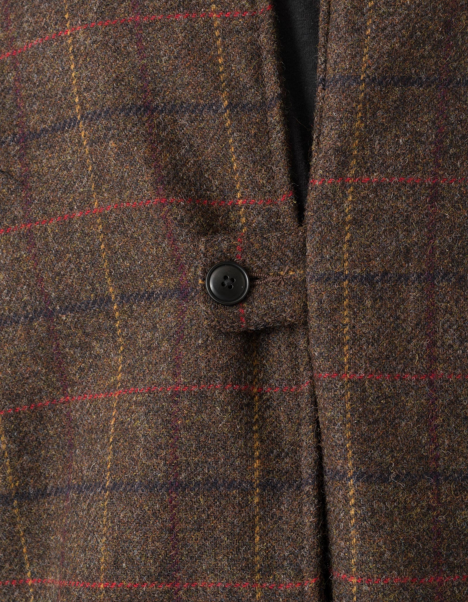 Close-up of a brown tweed coat with a button, featuring a plaid pattern.