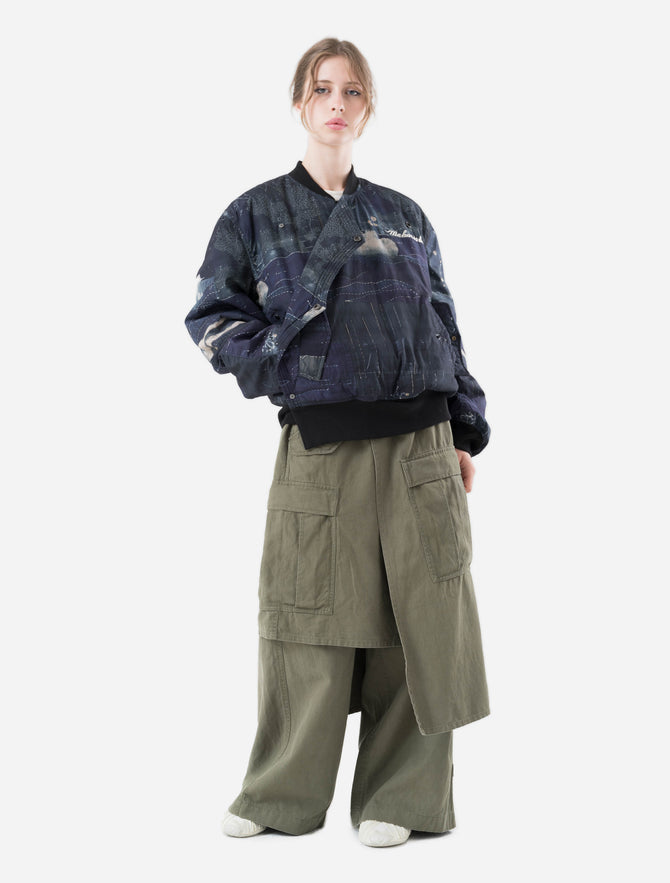 Person wearing a dark blue quilted maharishi jacket and green pants on a white background