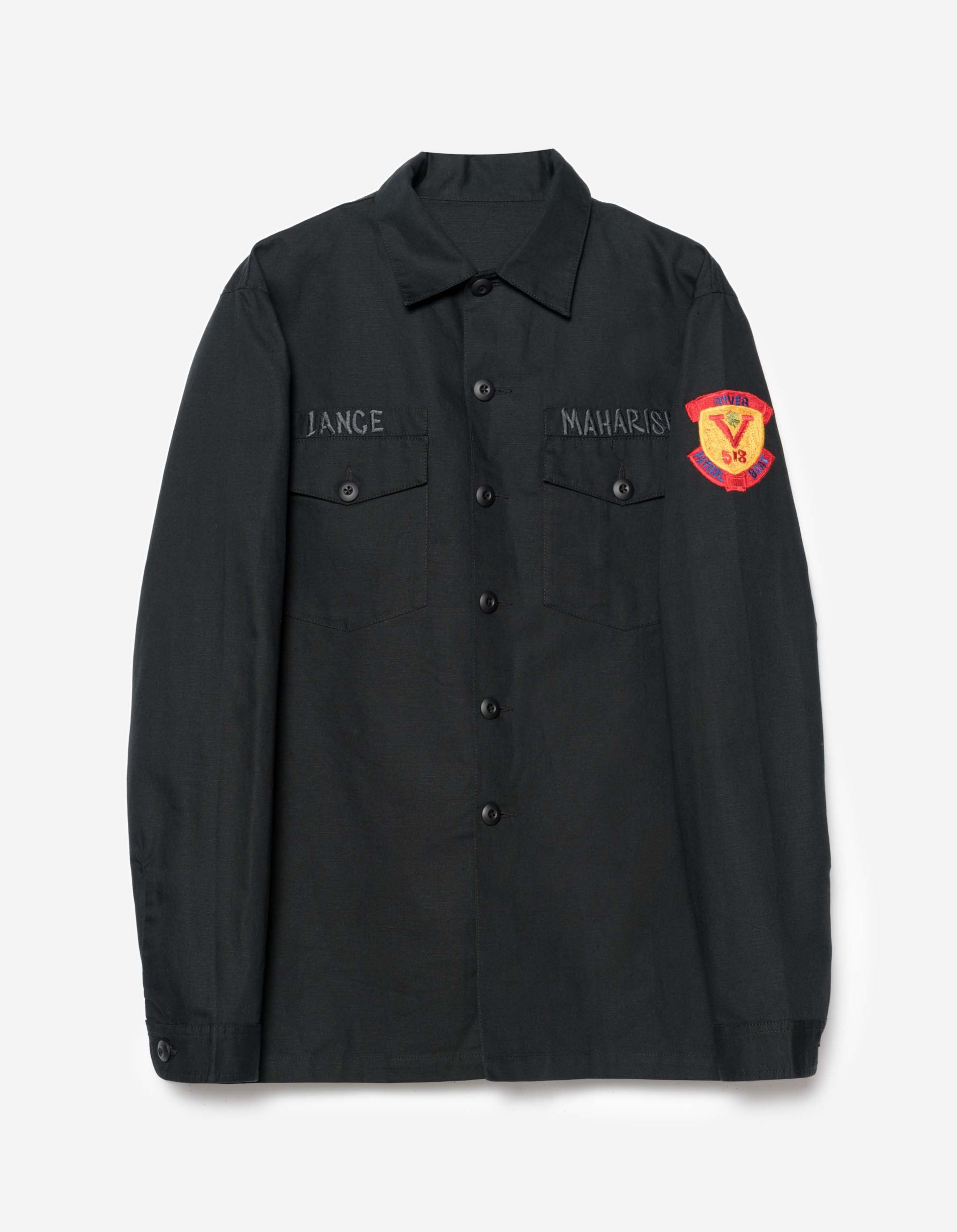 A long-sleeved black utility shirt with a button-up front, two chest pockets, and embroidery on the back. It features a shoulder patch and a woven nametape.