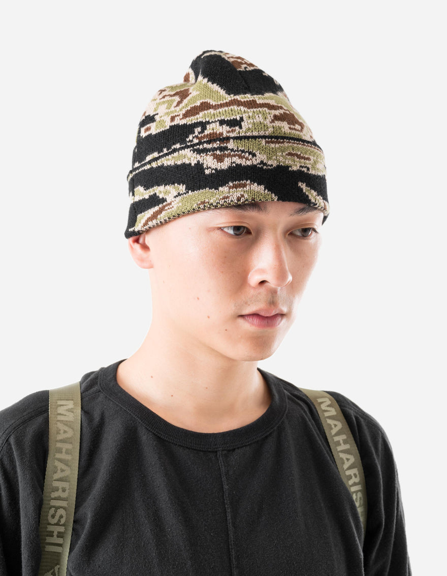 Person wearing a camouflage beanie and black shirt with 'MAHARISHI' branding.