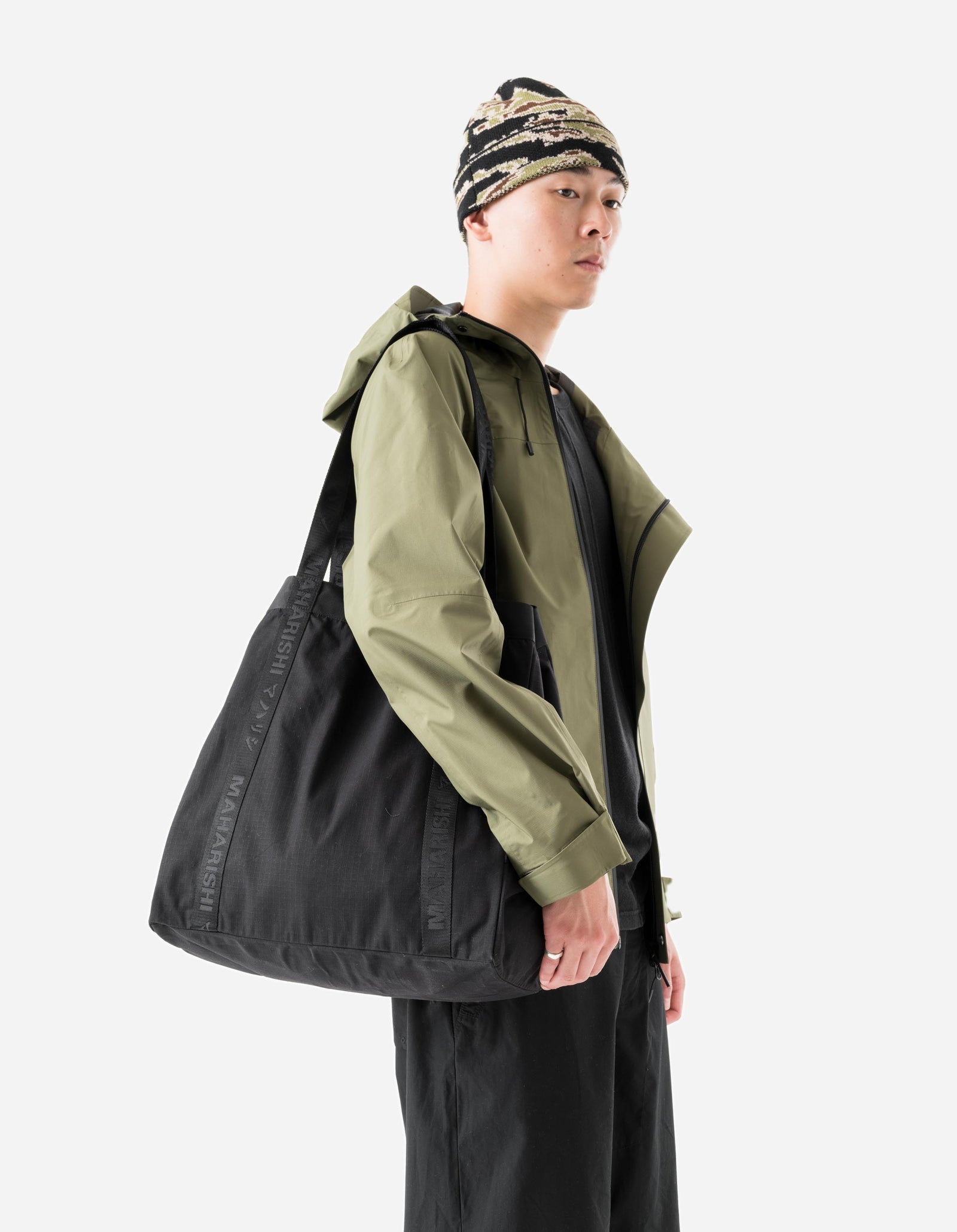Person wearing a green jacket and black pants with a black bag, standing against a white background