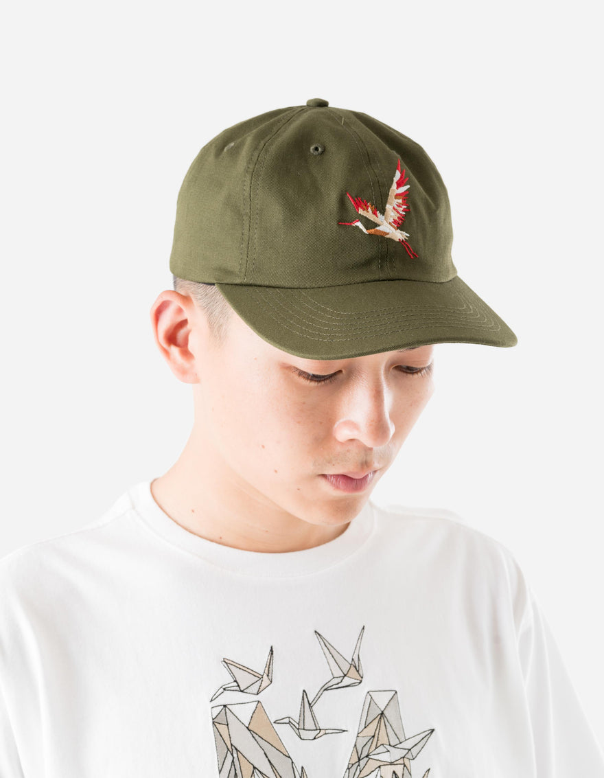 Person wearing an olive green cap with a red and white design on a plain background