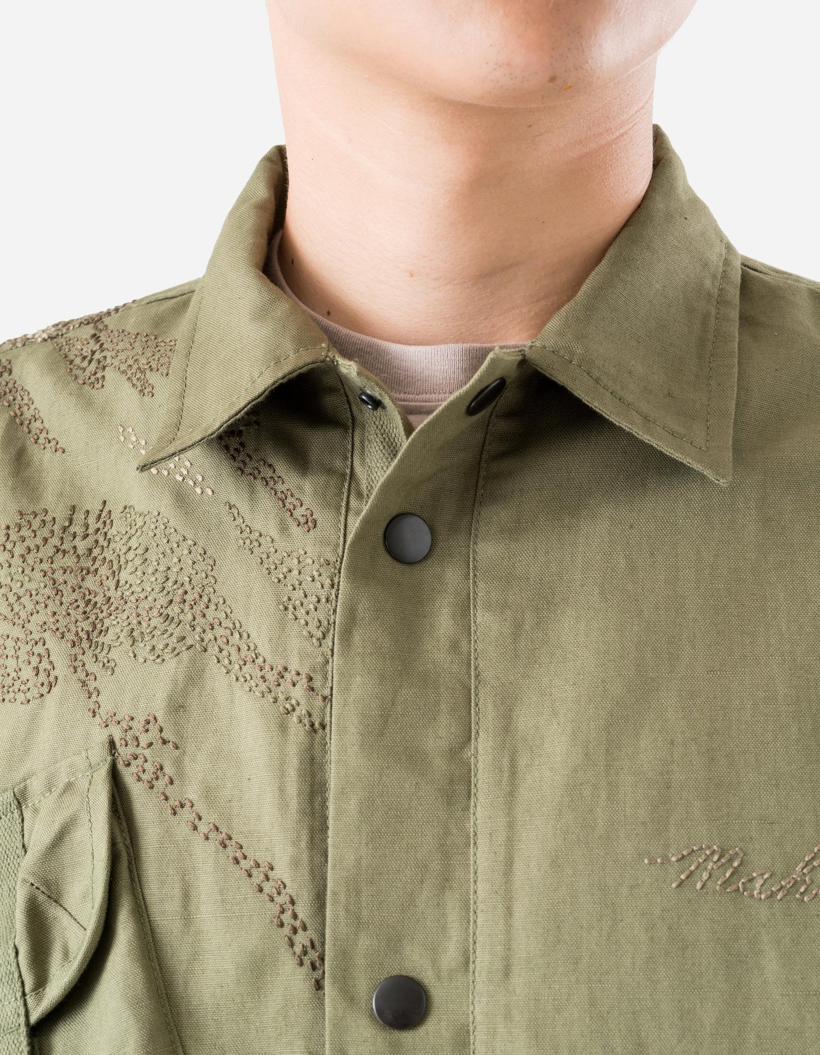 Close-up of a person wearing a green jacket with floral embroidery on a plain background