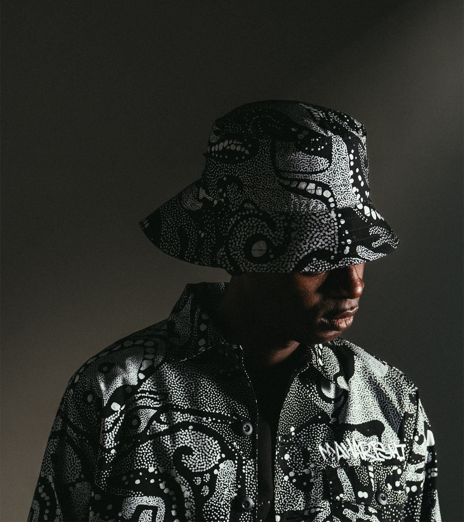 Person wearing a detailed mask and matching jacket against a dark background