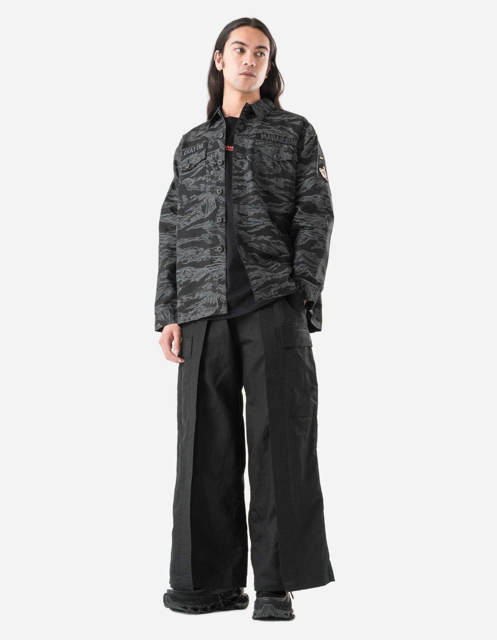 Person wearing a dark camouflage jacket and black pants on a white background