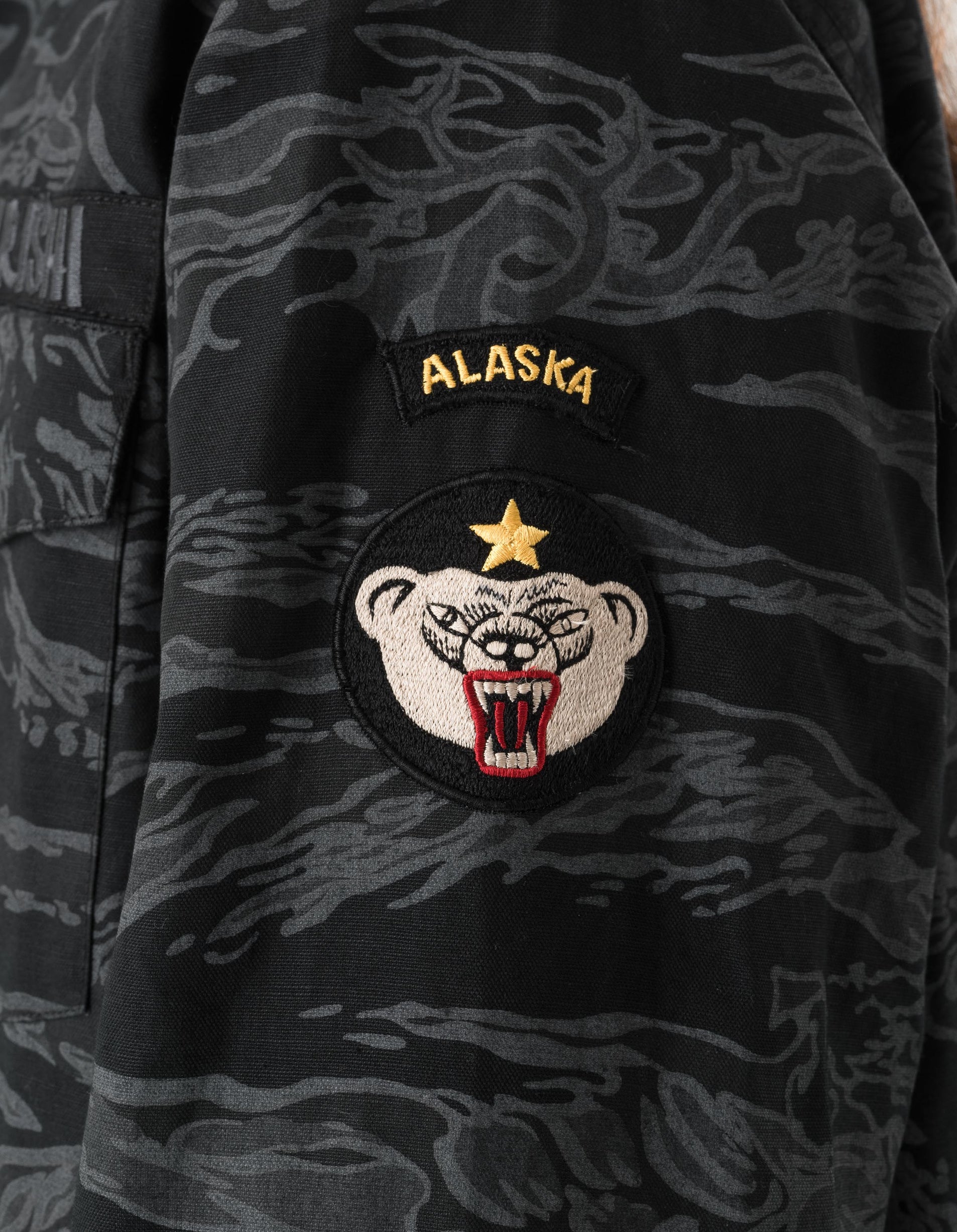 Camouflage jacket with an Alaska patch featuring a bear design.