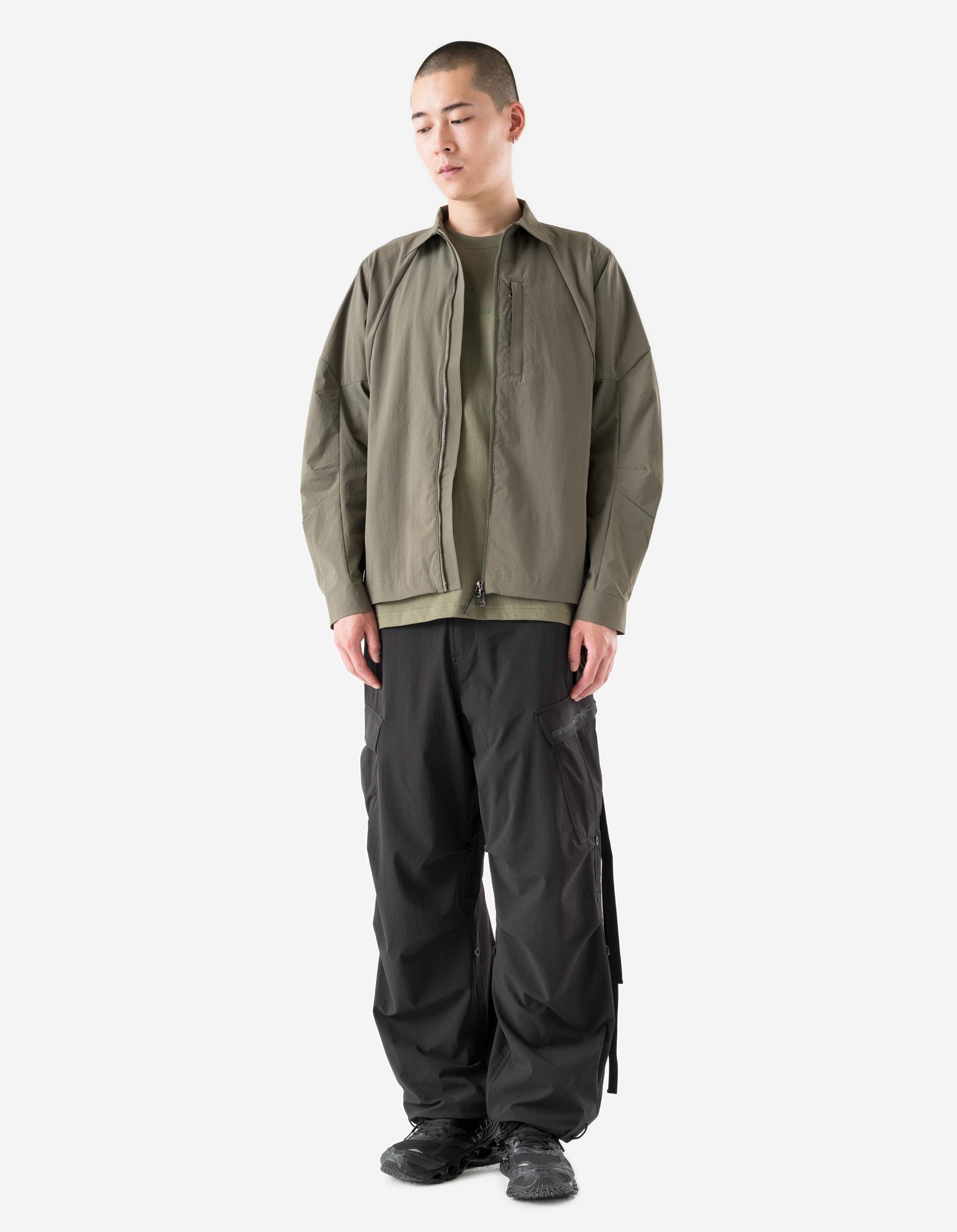 Person wearing a green jacket and black pants on a white background