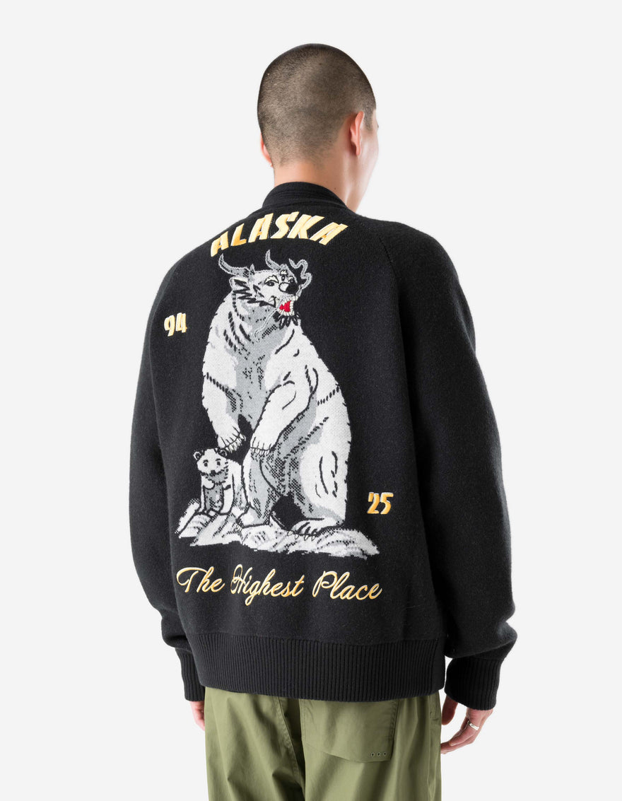 Person wearing a black jacket with a bear graphic and text on the back, on a white background
