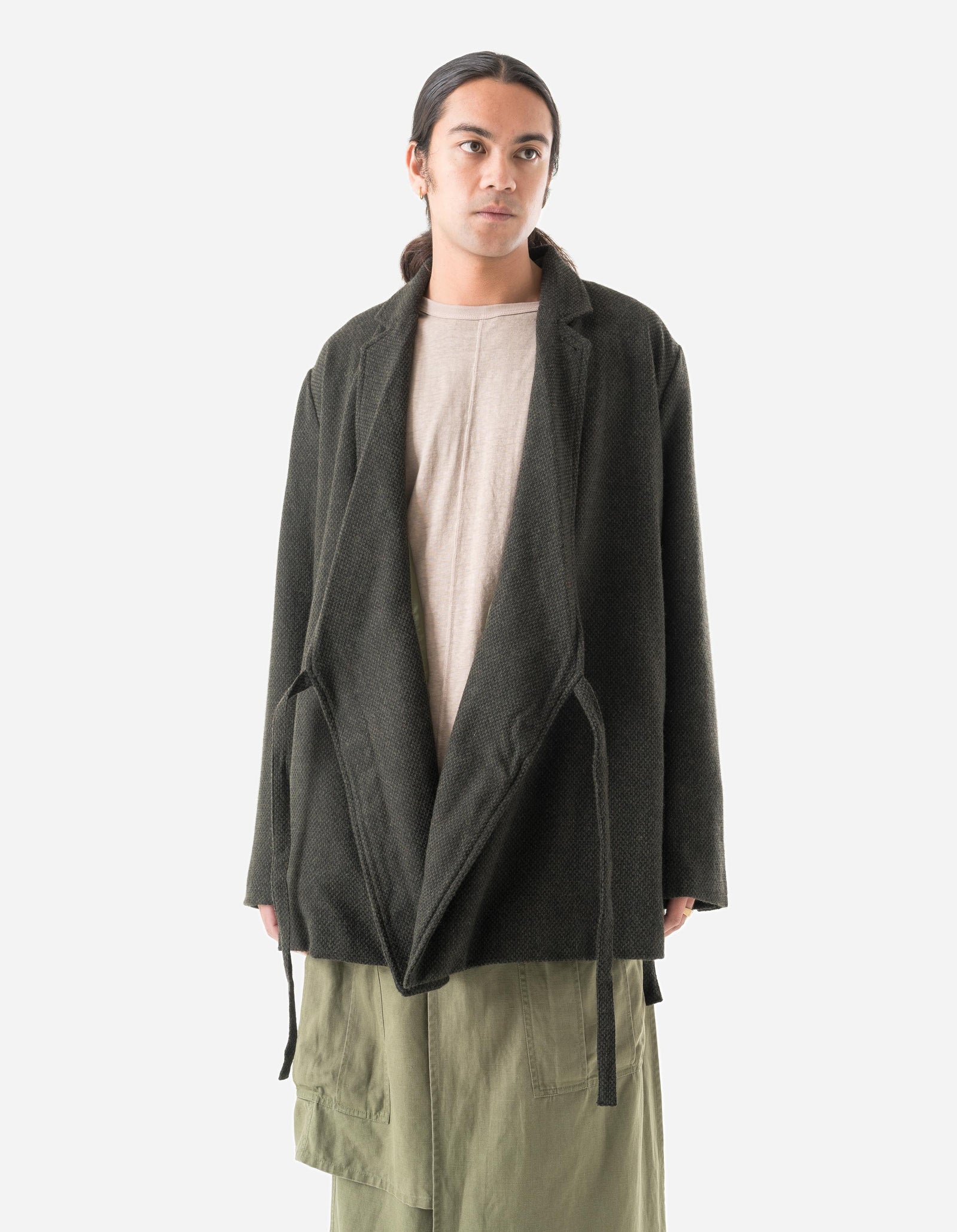 Person wearing a dark green coat over a beige shirt and light green pants on a white background