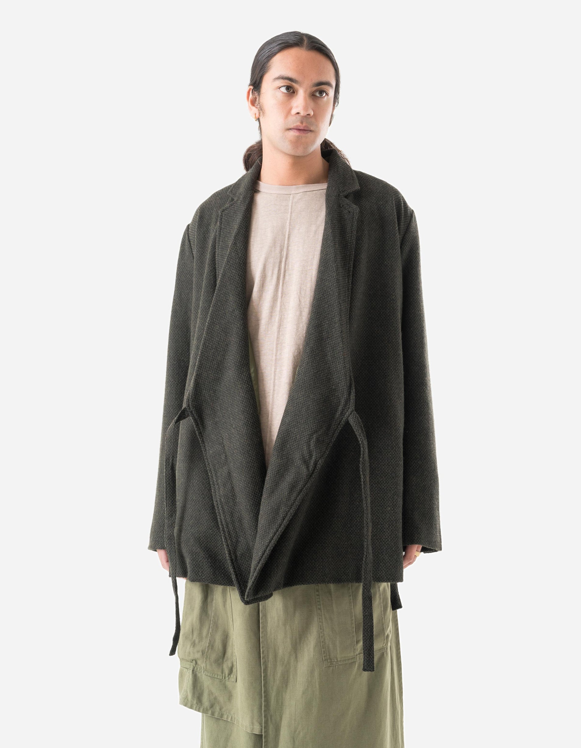 Person wearing a dark green coat over a beige shirt and light green pants on a white background