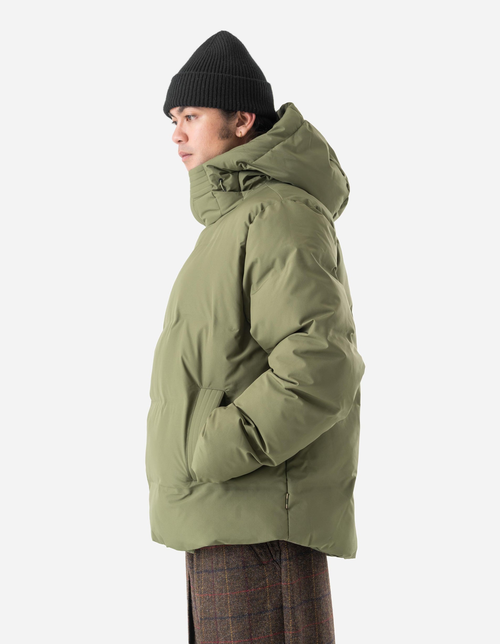 Person wearing a green hooded jacket and black knit cap on a white background