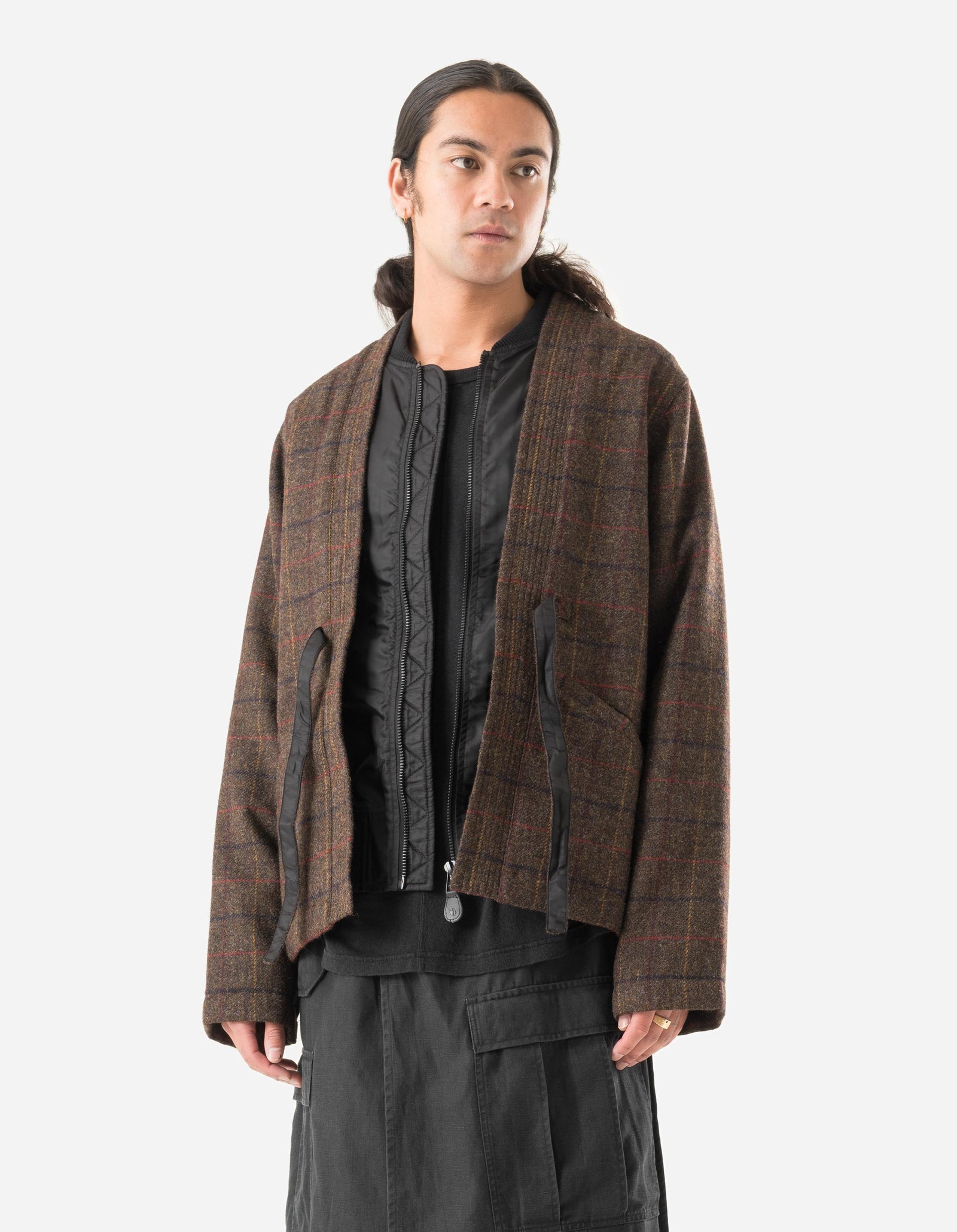 Person wearing a brown checkered jacket over a black shirt on a white background
