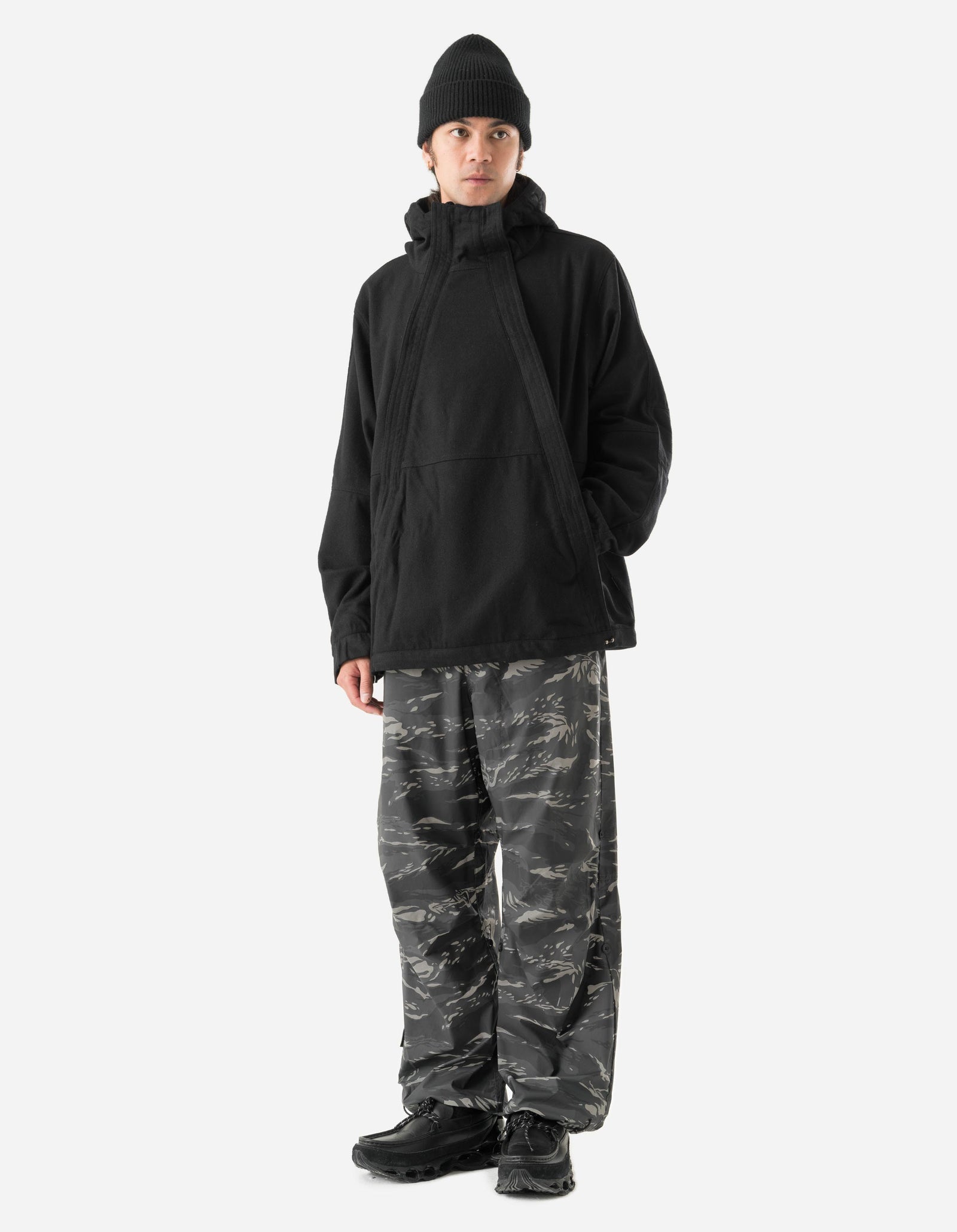 Person wearing a black jacket and camouflage pants on a white background
