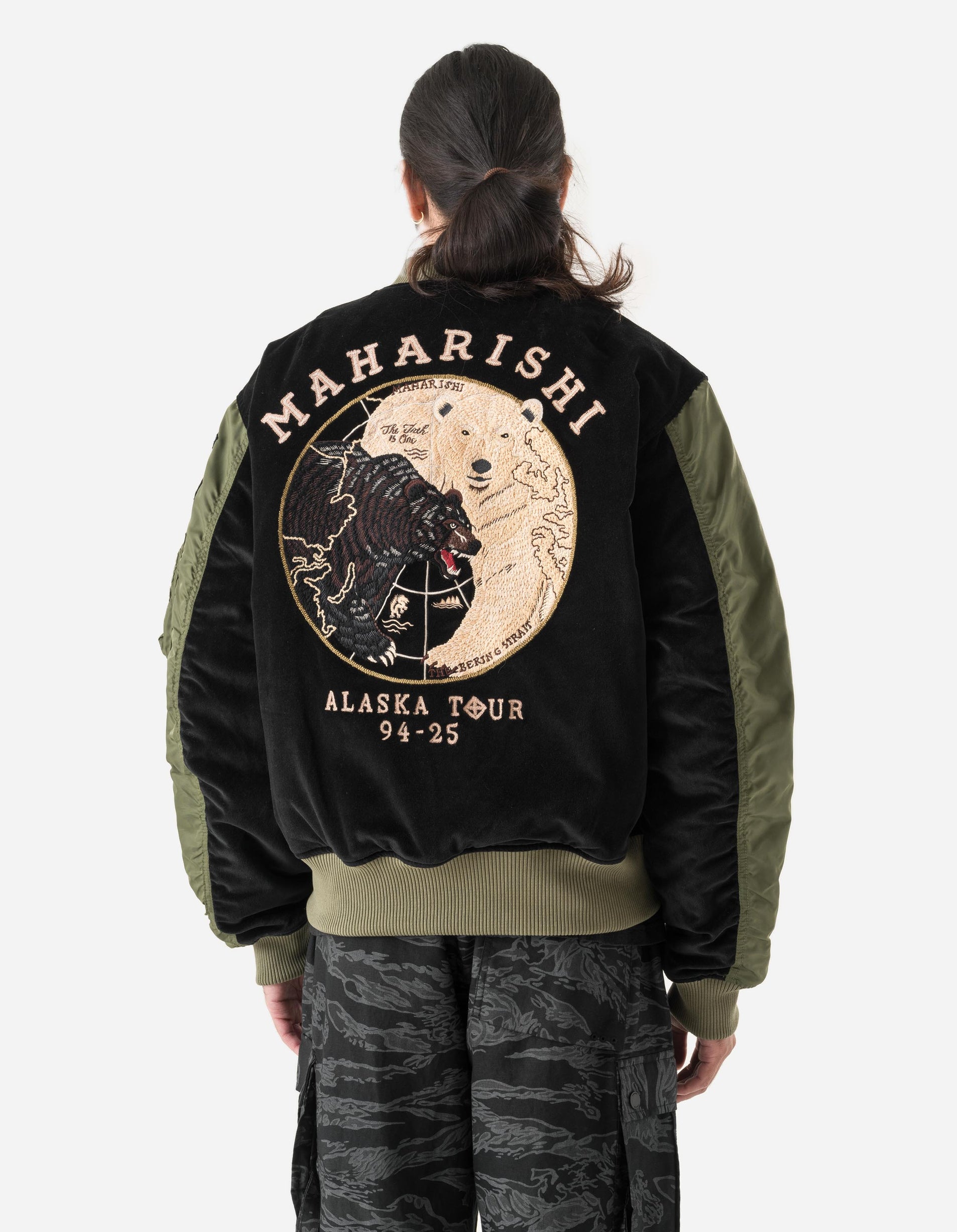 Person wearing a black Maharishi jacket with a graphic design on the back, standing against a white background.