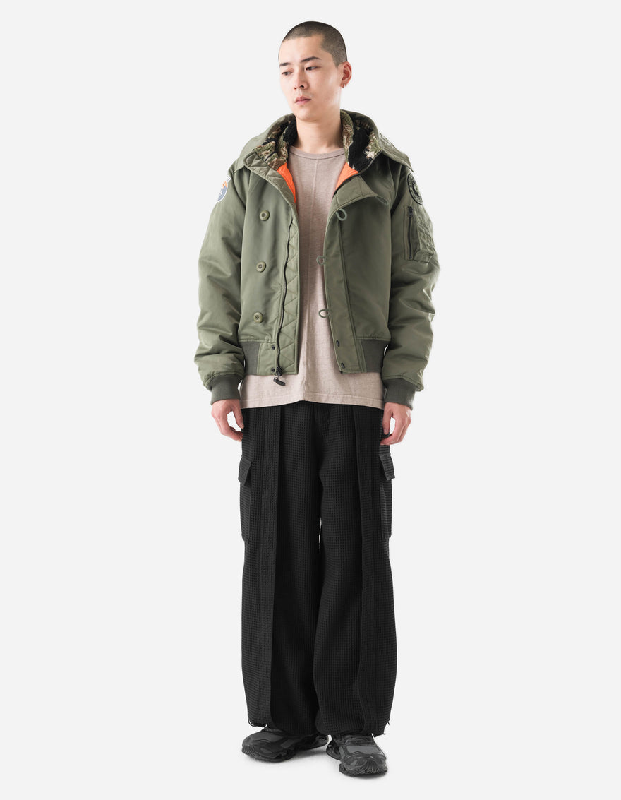 Person wearing a green jacket and black pants on a white background