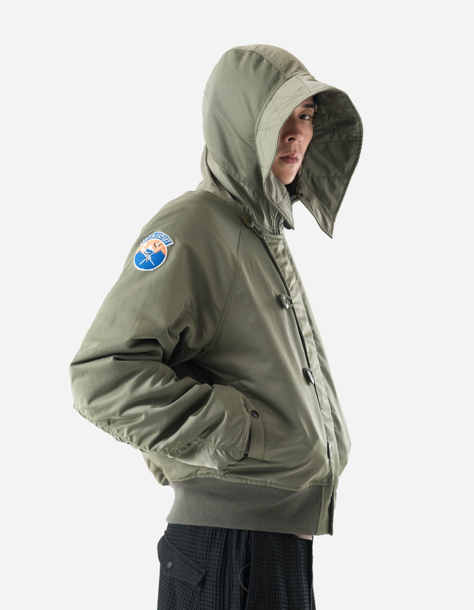 Person wearing a green hooded jacket with a logo on the sleeve against a white background