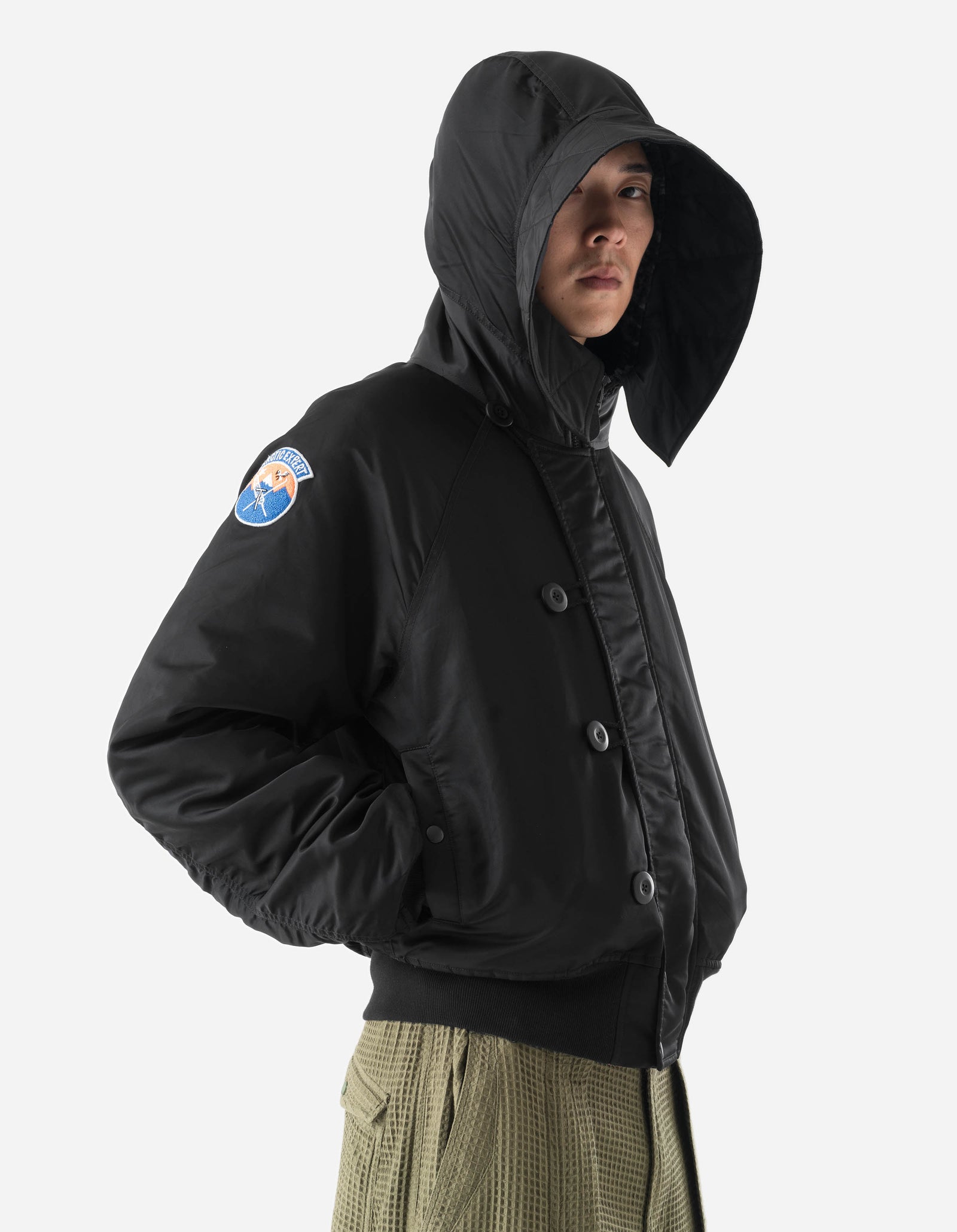 Person wearing a black jacket with a hood and a visible patch on a white background