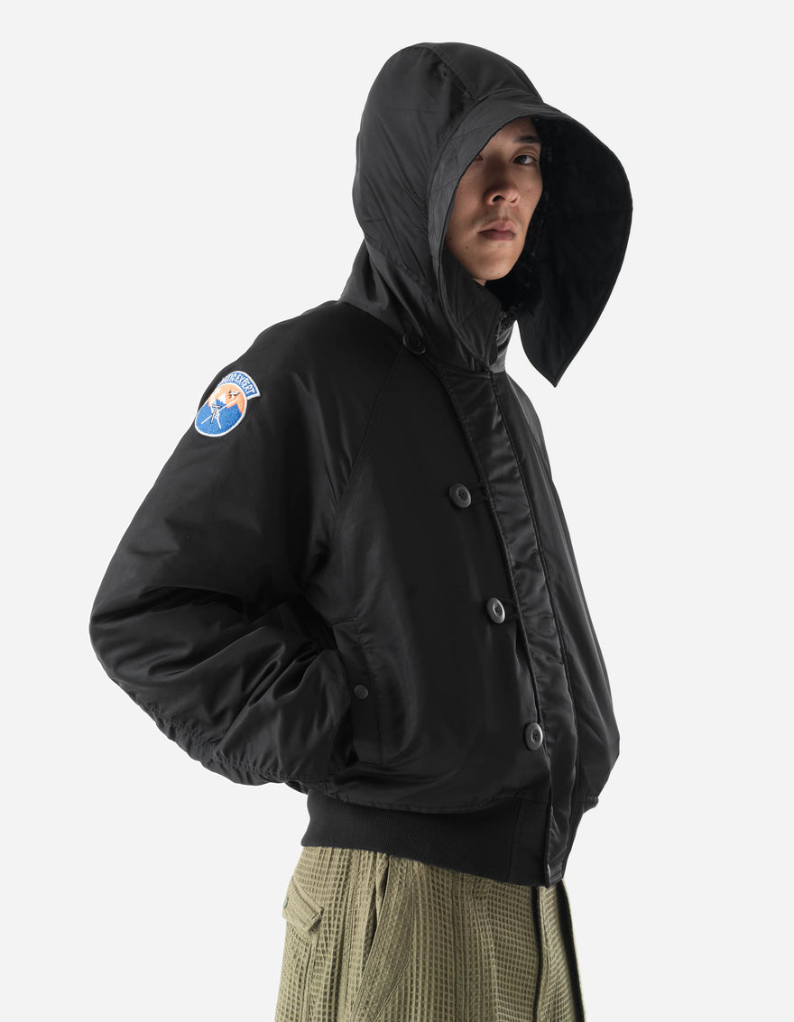 Person wearing a black jacket with a hood and a visible patch on a white background