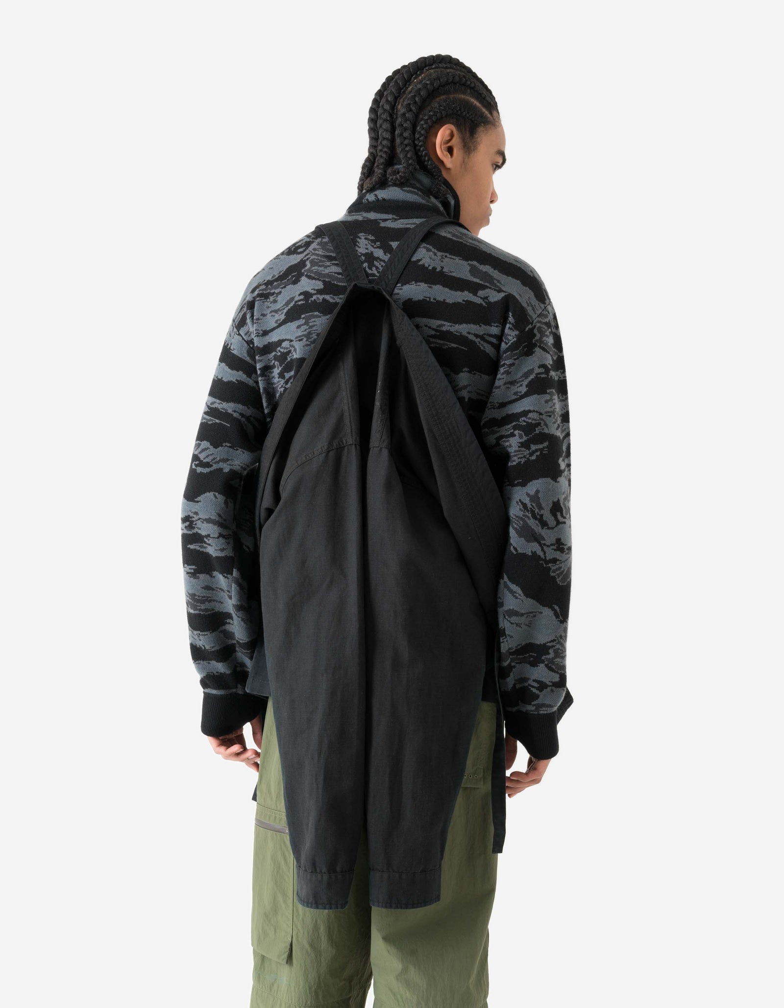 Person wearing a black and gray camouflage jacket with a black duffel bag over one shoulder on a white background