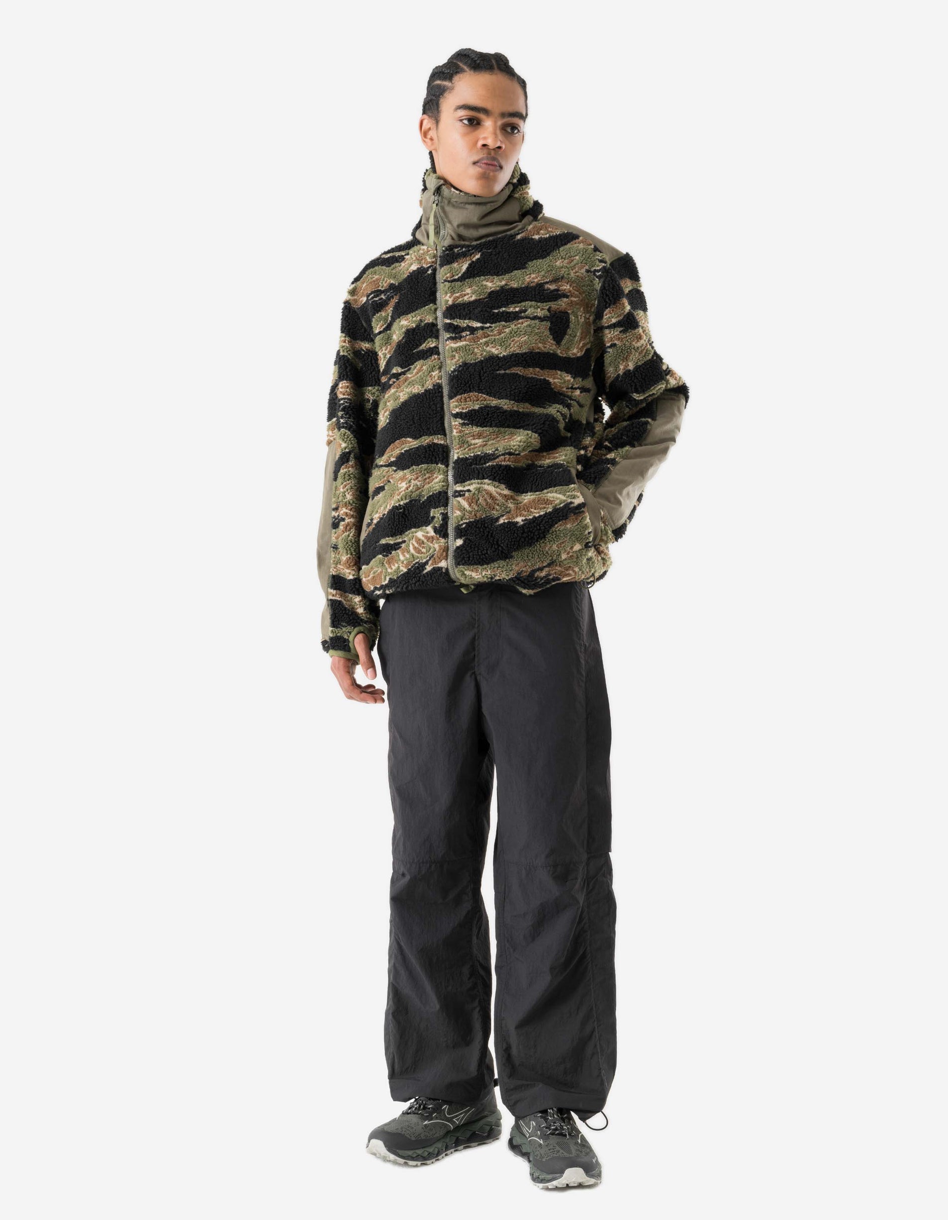 Person wearing a camouflage jacket and black pants on a white background