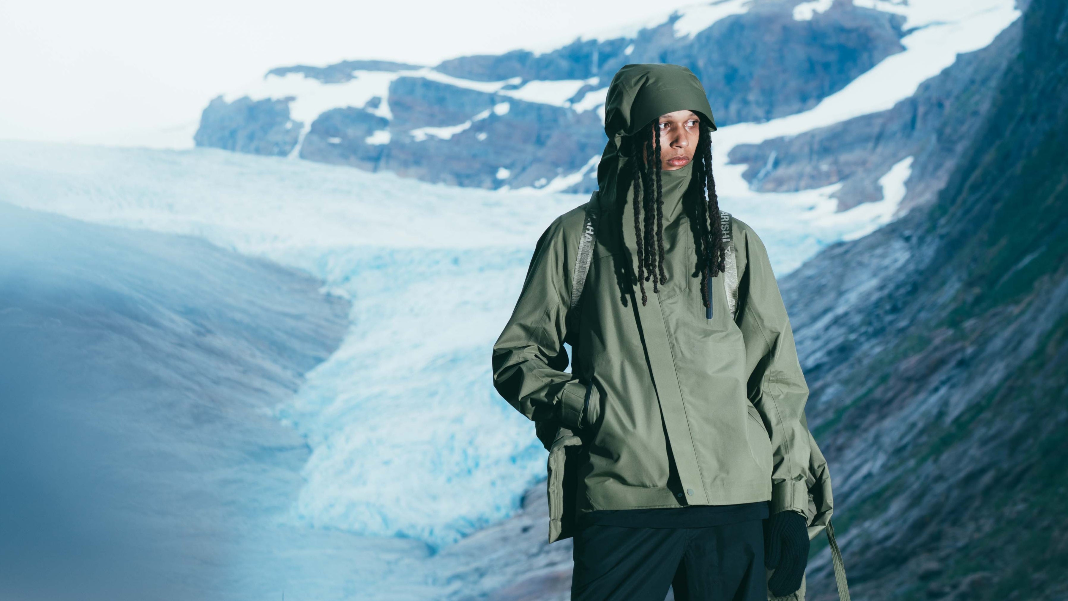 Person wearing a green raincoat standing in front of a glacier