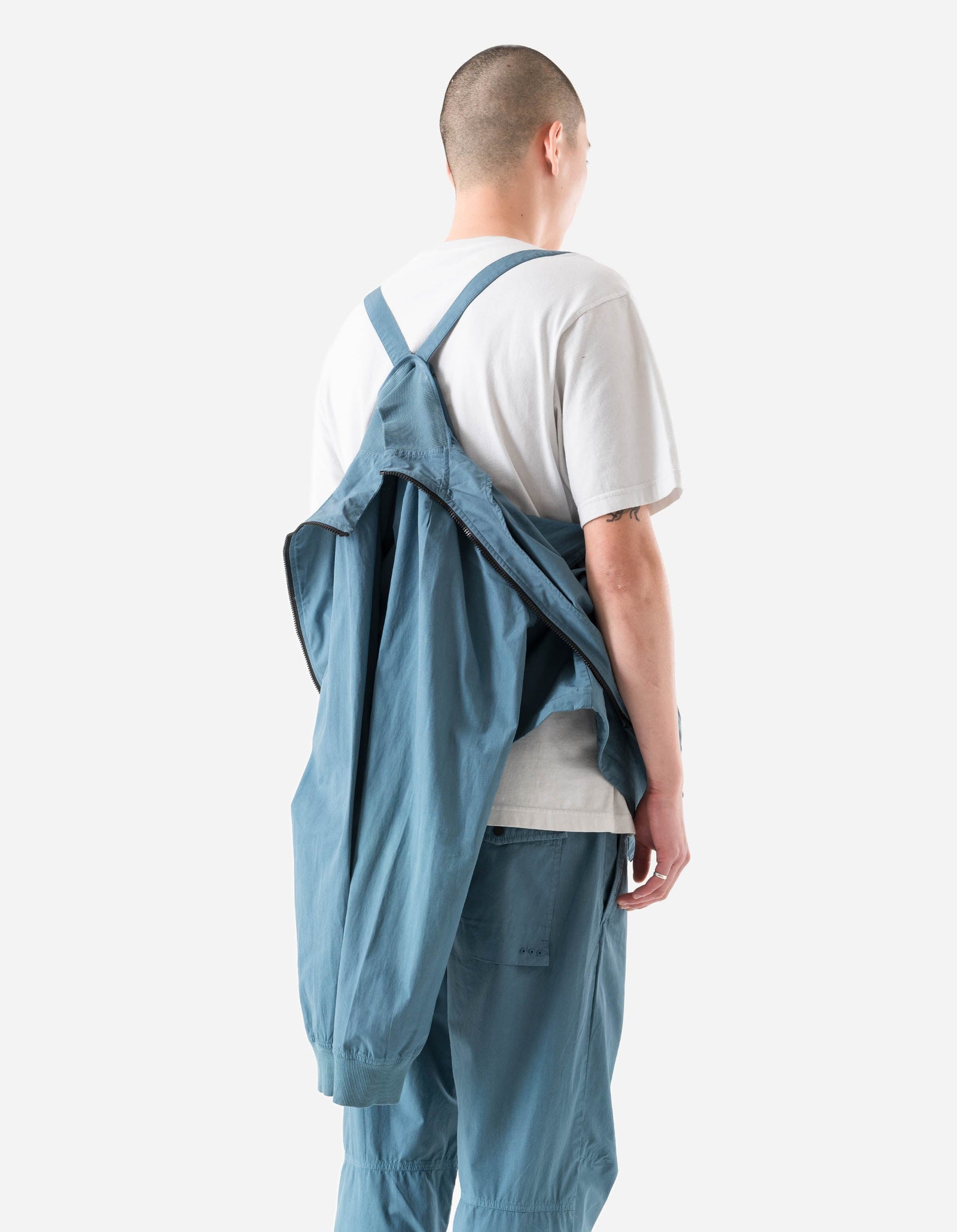 Person wearing blue overalls and a white shirt on a plain background