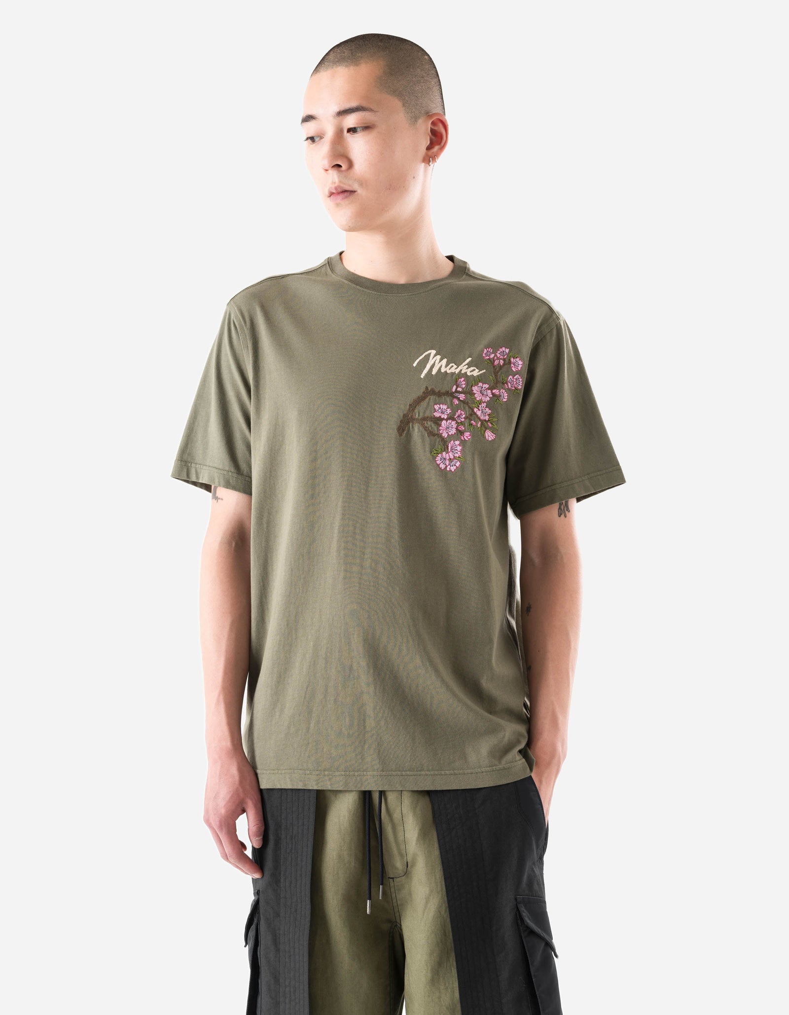 Person wearing an olive green t-shirt with floral design on a white background