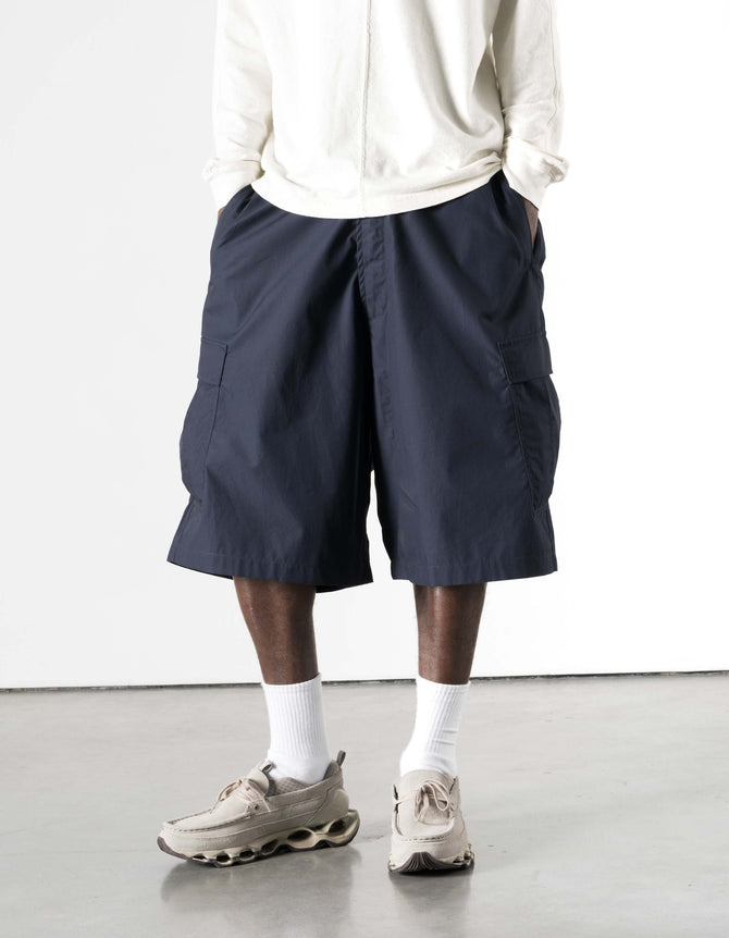 Person wearing navy shorts, white shirt, and beige sneakers on a light background