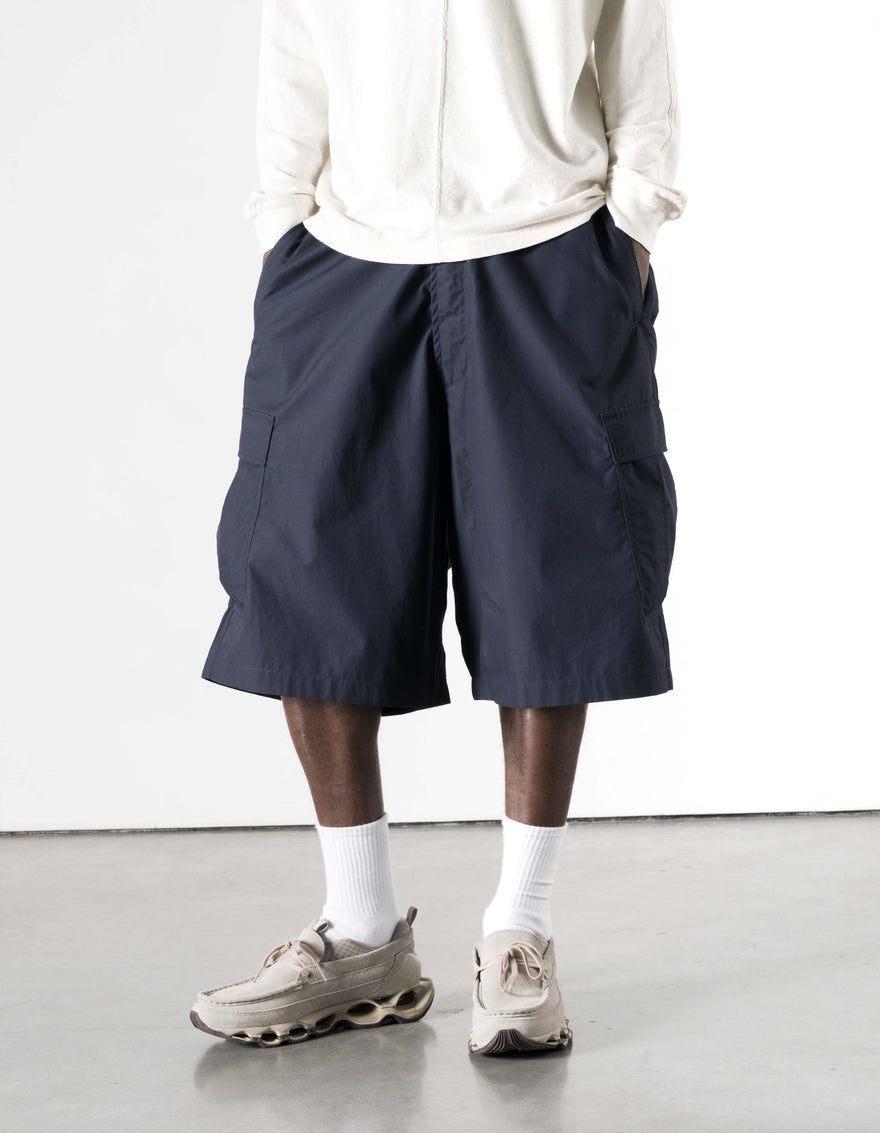 Person wearing navy shorts, white shirt, and beige sneakers on a light background