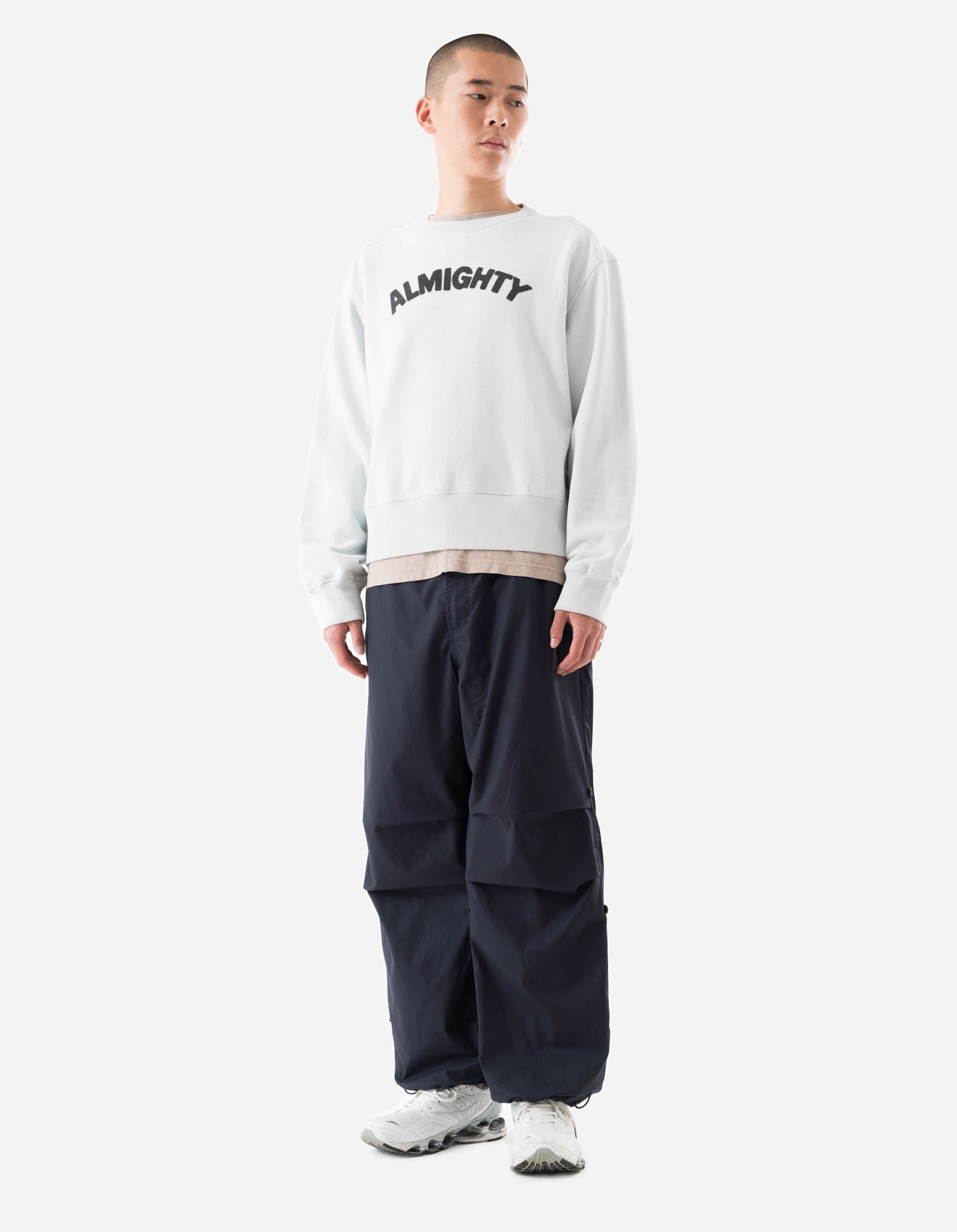 Person wearing a white sweatshirt with 'ALMIGHTY' text and dark pants on a white background