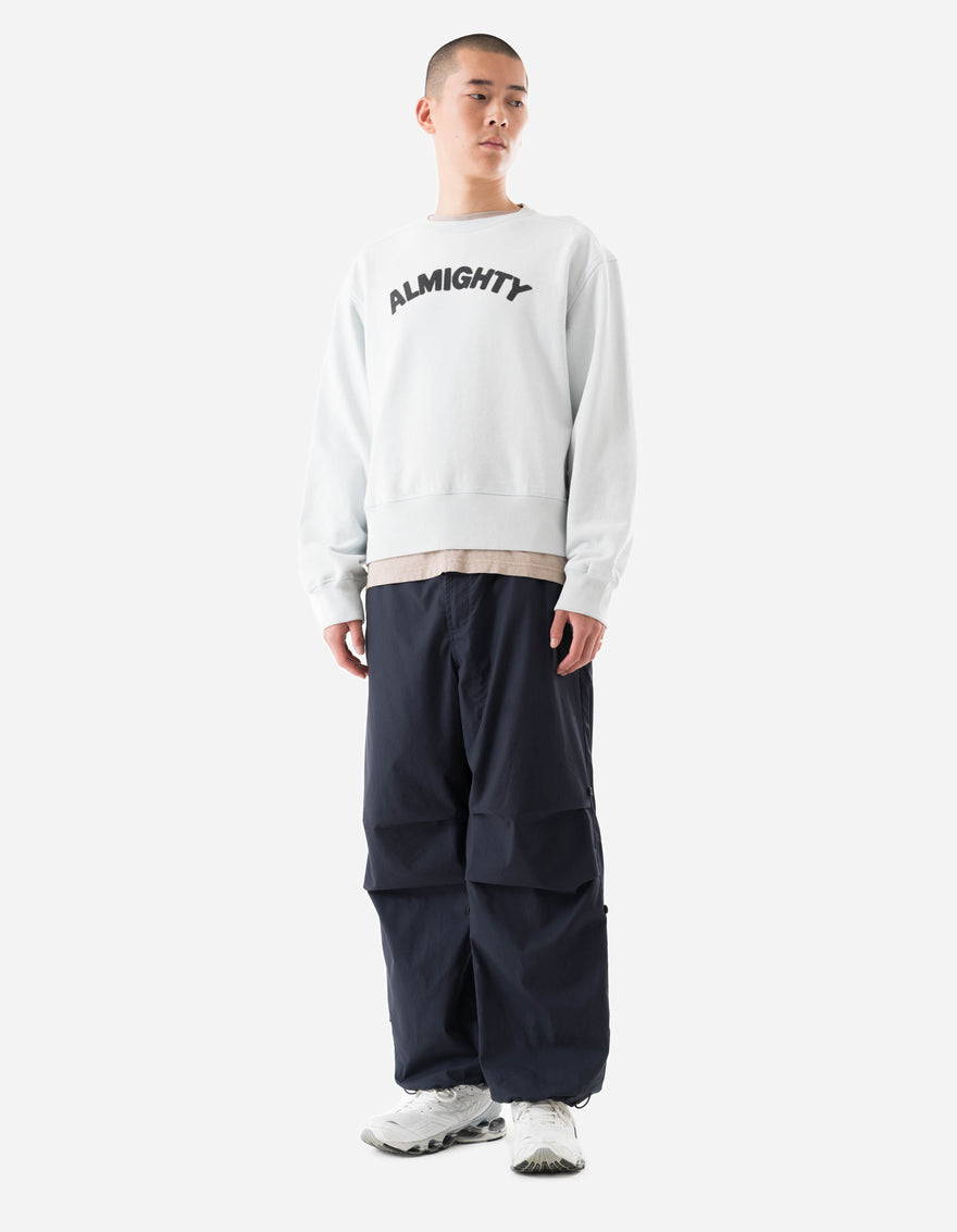 Person wearing a white sweatshirt with 'ALMIGHTY' text and dark pants on a white background